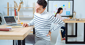 Mann som sitter får smerte i ryggen.